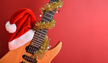 Kırmızı izole edilmiş arka planda Noel Baba şapkası olan elektro gitar gövdesi. Noel gitarı müzik konsepti.