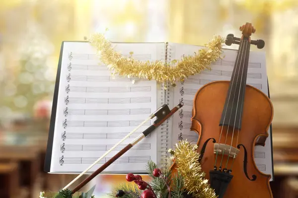 Christmas religious violin music concept with violin with christmas decoration and sheet music with religious temple background. Front view.