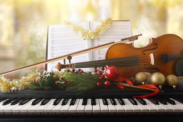 Christmas religious music concept with piano and violin with christmas decoration and sheet music with religious temple background. Front view.