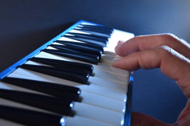 Mavi arkaplan ve ışık demeti aydınlatan mavi melodiyi çalan elin ayrıntıları.