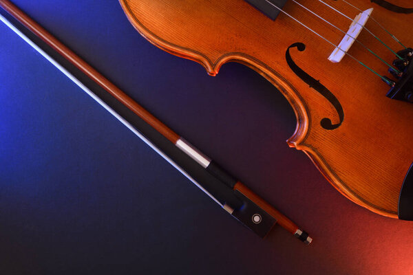 Detail of traditional stringed violin body and bow on black background with red and blue lights. Top view.