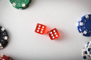 Kumarhane zar oyunu arka planında ortada iki kırmızı zar ve ucunda da beyaz masada izole edilmiş farklı renkte bahis çipleri var. Üst görünüm.