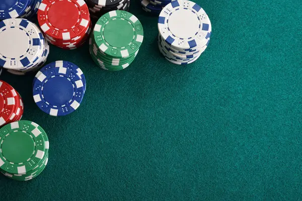 Detail of casino gaming background with stacks of betting chips of different in a corner of the image on green gaming mat. Top view.