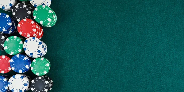 Casino gaming background with stacks of betting chips of different colors on the left of the image on green gaming mat. Top view.