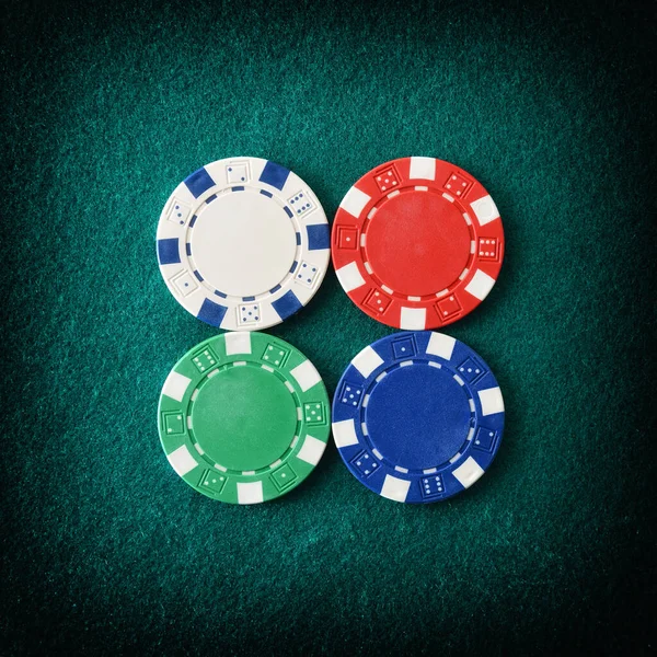 Casino background with detail of four different colored plastic chips centered on green felt gaming mat. Top view. Square composition