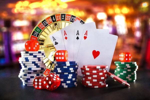Casino games background with playing cards, betting chips and dice for playing various games of chance on black table and game room background. Front view.