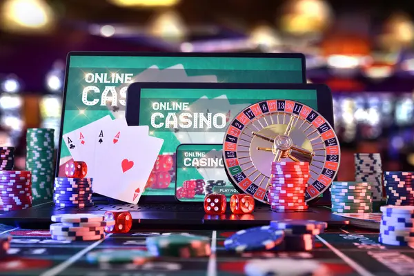 Electronic devices for online casino game with app on screen on gaming table with chips, cards, dice and roulette in a gaming room. Front view.