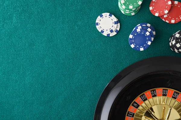 Casino roulette background on green felt mat and betting chips in a corner. Top view.