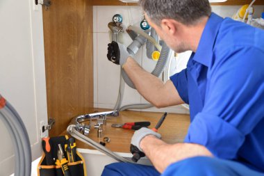 Detail of plumber in uniform repairing a leak under the sink in a home with tools around. Horizontal composition.