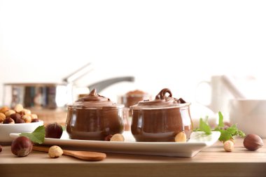 İki cam kavanoz dolusu kakao kremalı, fındıklı, yapraklı ve fındıklı, ahşap mutfak tezgahında, izole edilmiş arka planda. Ön görünüm.