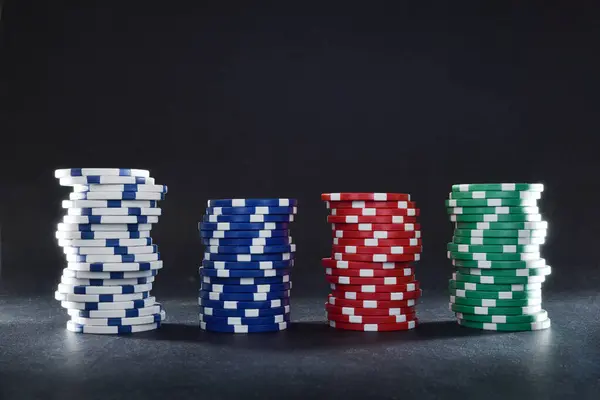 Various stacks of casino game bet chips of various colors on black table and black isolated background. Front view.