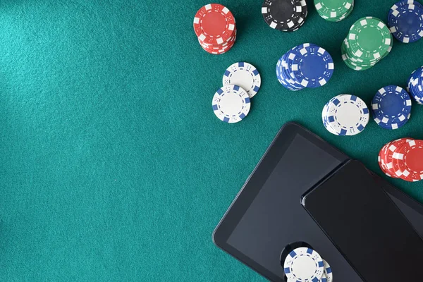 Concept of playing casino games online with mobile devices on a game table with green felt full of game objects. Top view.