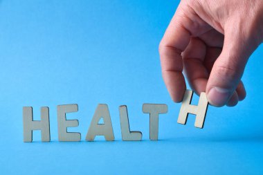 Sağlık mesajı, mavi arka planda ahşap harf kesikleriyle sağlık kelimesini besteliyor. Ön görünüm