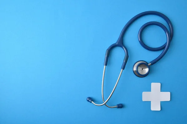 General medicine concept with stethoscope and white paper cross-shaped on blue background. Top view