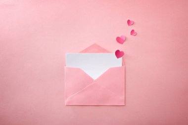 Pembe desenli arka planda kalp kesikleri olan boş beyaz çarşaflı açık pembe bir zarf. Üst görünüm.