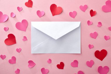 Ortasında pembe arka planda pembe ve kırmızı kalplerin olduğu beyaz bir zarf var. Üst görünüm.