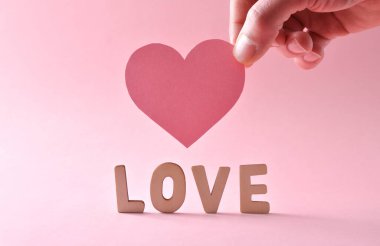 Aşk arkaplanı, pembe arka planda sevgi ve el ele tutuşan kalp kesikleri oluşturan harf kesikleriyle dolu. Ön görünüm.