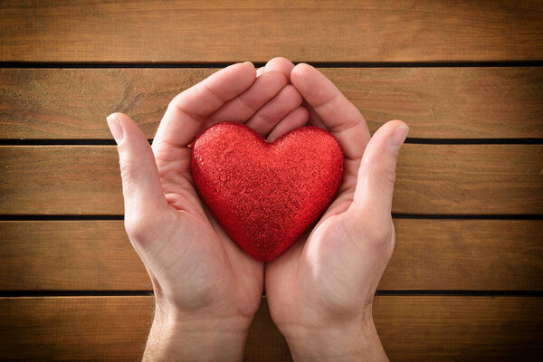 Блестящее сердце между руками мужчины на деревянном столе. Вид сверху.