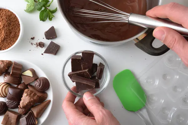 Person making homemade chocolate bonbons on white kitchen bench at home with ingredients and kitchen utensils. Top view.