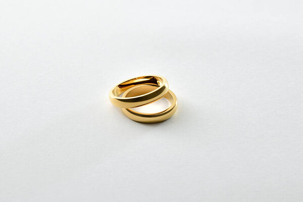 Detail of overlapping gold engagement rings isolated on white textured base. Elevated view.