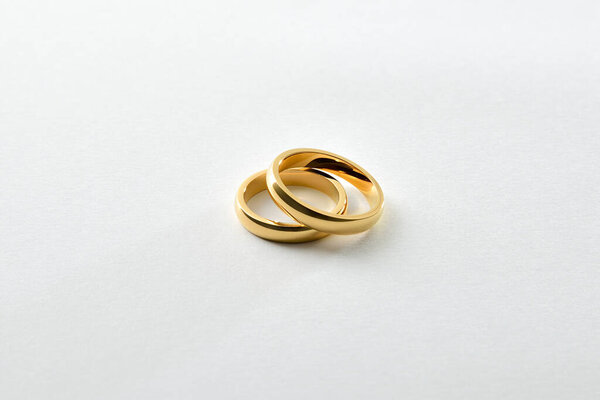 Detail of overlapping gold engagement rings isolated on white textured base. Elevated view.