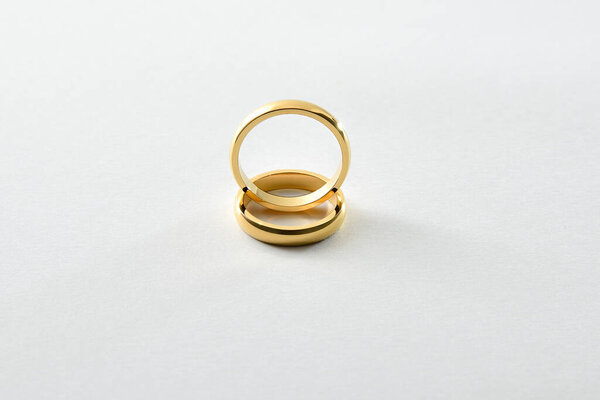 Detail of engagement gold ring standing on each other on white textured base. Elevated front view.