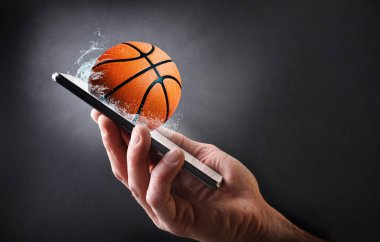 Elle tutulan cep telefonuyla basketbol izleme kavramı top ve koyu gri izole edilmiş arka plan.