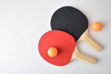 İki masa tenisi raketi ve beyaz masada izole edilmiş iki turuncu top. Üst görünüm.