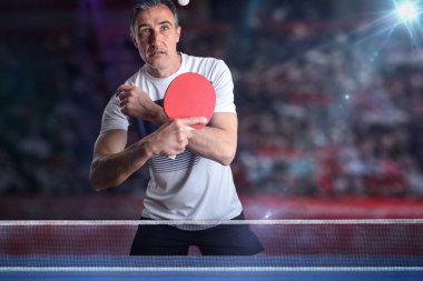 Özenli pinpon oyuncusu arka planda duran bir sergide mavi bir oyun masasının arkasında beyaz bir top alıyor..