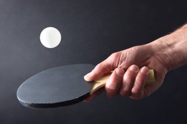 Masa tenisi oyuncusunun siyah izole edilmiş arka planda siyah lastik parçasıyla beyaz bir topa vurması. Ön görünüm.