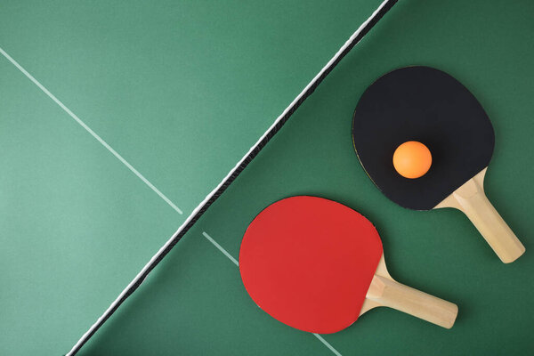 Set of ping pong paddles and orange ball on green playing table. Top view.