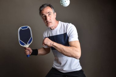 Profesyonel bir picleball oyuncusunun, izole edilmiş gri arka planda beyaz bir topa vurmasının ayrıntıları.
