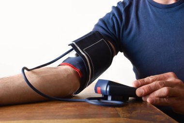 Evdeki ahşap masada dijital bir sayaçla kan basıncı ölçen bir adam. Yan görünüm.