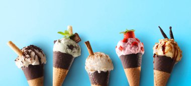 Arka arkaya beş farklı aromalı dondurma külahı ve mavi arka planda çikolata..