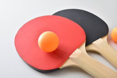 Masa tenisi raketleri ve beyaz masada izole edilmiş iki turuncu top. Yüksek görünüm.