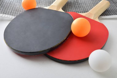 Masa tenisi raketleri, beyaz masada izole edilmiş ağ ve turuncu top seti olan bir arka plan. Yüksek görünüm.