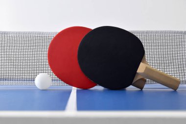Ağ üzerinde duran raketlerle pinpon seti ve beyaz topla mavi oyun masası manzarası. Ön görünüm.