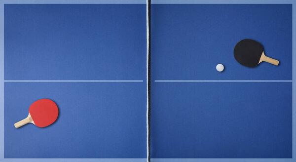 Top view of professional blue ping pong playing surface with paddles on each side and ball. Top view.