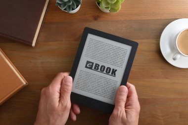 Evdeki ahşap bir masada rahatça kitap okuyan kişi. en üstteki görünüm