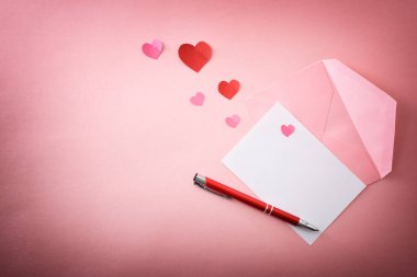 Kalem ve kalp şeklinde kağıt kesikleri olan pembe bir zarfın üzerindeki boş mektup. Üst görünüm.