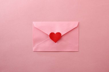Pembe arka planda kırmızı kalp kesiği olan kapalı pembe zarflı bir arka plan. Üst görünüm.