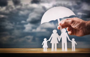 Aile koruma kavramı, ahşap bir tabanda şemsiyesi olan bir aileyi ve arka planda yağmurlu bulutları kaplayan bir el kaplaması...
