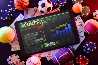 Farklı spor, para ve bahis fişlerini temsil eden nesnelerle siyah bir masanın ortasında, tabletle online spor bahisleri. Üst görünüm.