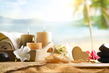 Ahşap bir masada, mumlarla, havlularla ve arka planda plajlı çiçeklerle, ürünlerle ve dekoratif elementlerle vücut ve zihin sağlığıyla. Ön görünüm.