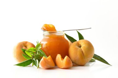 Beyaz arka planda izole edilmiş şeftali reçeli kavanozu ve tabanda da meyve ve kaşık var. Ön görünüm.