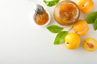 Erik reçelli kavanozlar beyaz masada yalıtılmış, meyveli ve yapraklı. Üst görünüm.