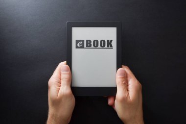 Ekranda yazılı bir kitap ve izole edilmiş siyah bir arkaplan tutan eller. Üst görünüm