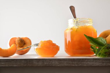 Kavanoz ve kase şeftali reçeli ve meyve parçaları ve ahşap masa üzerinde yapraklı dilimler izole edilmiş arka plan. Ön görünüm.