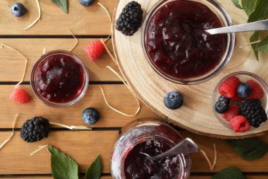 Ahşap tabaklarda cam kaplarda doğal böğürtlen reçeli ve meyve ve yapraklarla dolu kırsal masa. Üst görünüm.