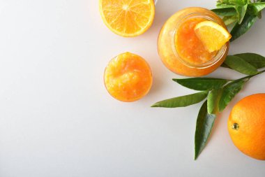 Turuncu marmelatlı kavanozlar beyaz masada yalıtılmış, meyveli ve yapraklı. Üst görünüm.